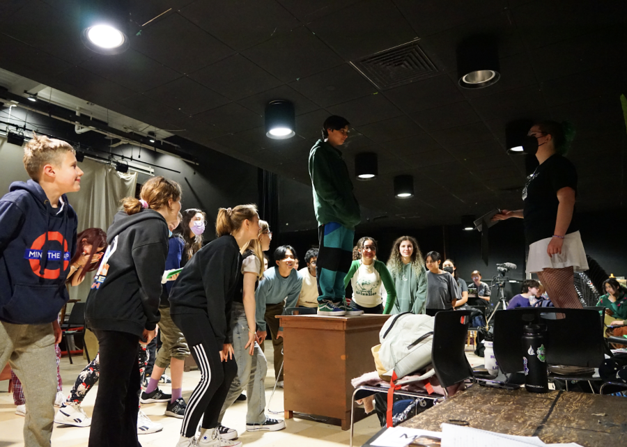 Actors huddle around a desk while rehearsing a dance piece. (Source: Alex Strand (I))