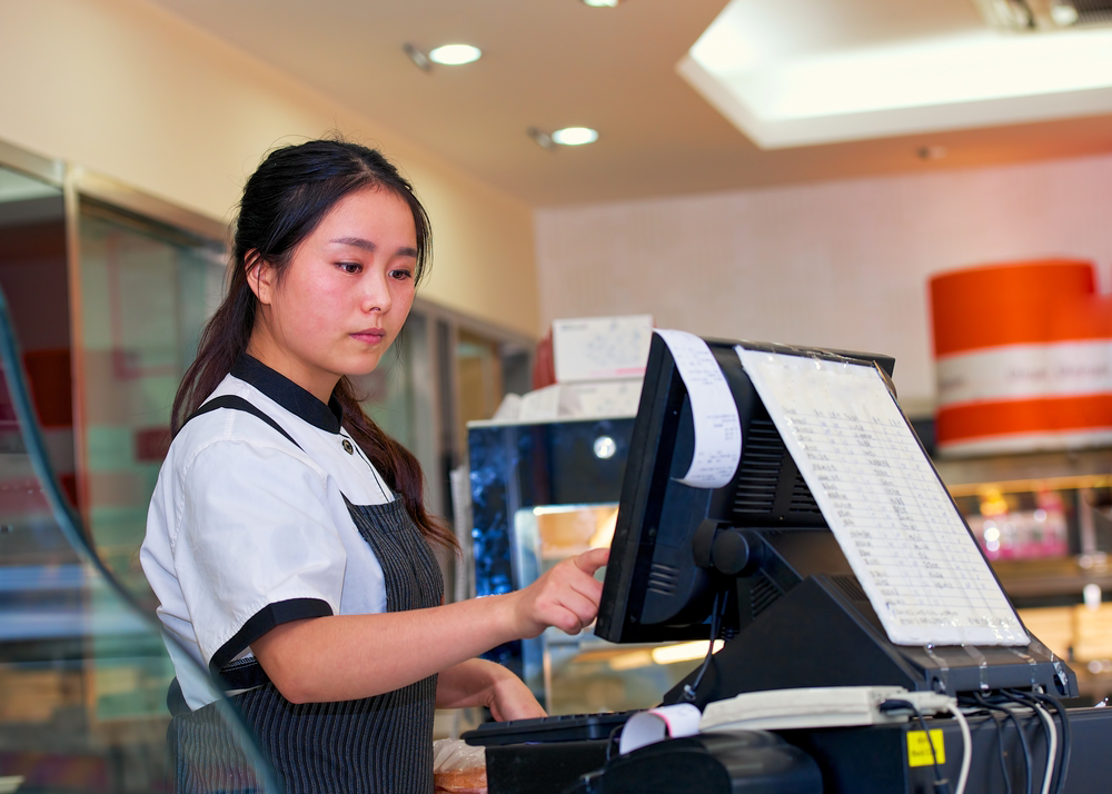 This worker enters a sale on the cash register. (Source: Shutterstock)